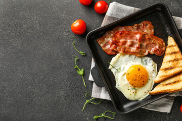 Composition with frying pan of tasty fried egg, bacon, toasts and tomatoes on dark background