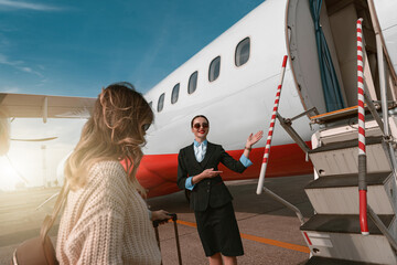 Woman stewardess standing near airplane and inviting female passenger on board