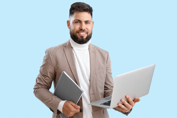 Handsome teacher of computer sciences with laptop and notebook on blue background