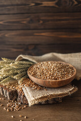 Ears of wheat and bowl of wheat grains on brown wooden background