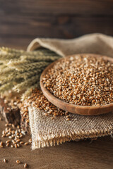 Ears of wheat and bowl of wheat grains on brown wooden background