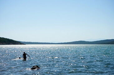 Badegäste im seichten Wasser in der Bucht vor Ayvalik im Sommer bei blauem Himmel und Sonnenschein...
