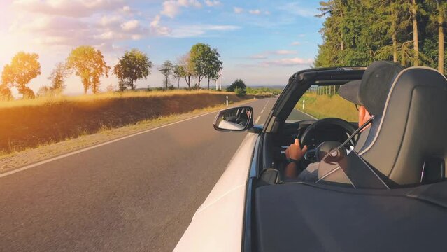 Adult man is driving with convertable car in sunny nature on a bright summer day. wide angle pursuit shot