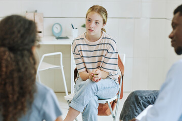 Portrait of young teenage girl in support group circle listening to kids sharing story in mental...