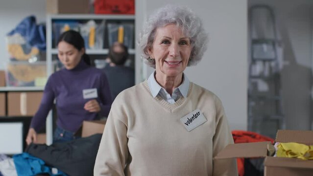 Portrait of senior woman volunteer pack donated clothes in volunteering center