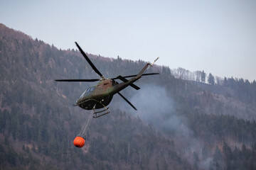 Obraz na płótnie Canvas The helicopter carrying a bucket to deliver water for aerial firefighting in a mountain forest