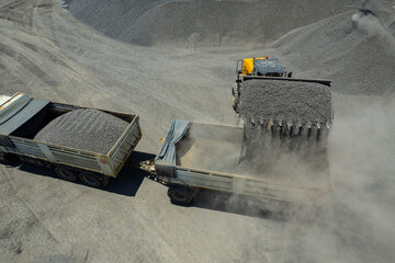 Sand loaders are shoveling rocks into dump trucks.