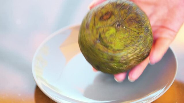 Macro closeup of one ripe soft diospyros nigra black sapote on white plate with hands touching putting chocolate pudding soapapple zapote prieto tropical fruit