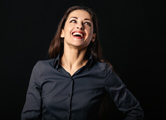 Beautiful thinking toothy laughing business woman with folded arms in blue shirt on black background with empty copy space. Closeup