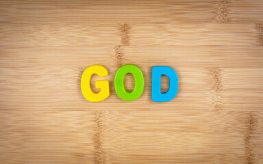 The word god is laid out of multicolored letters on a table background with a wood texture. Concept. Christianity. God