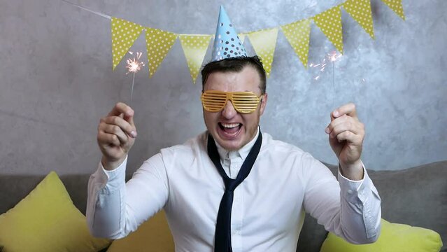 Loud smiling man happy birthday. Very happy young man celebrating a birthday, a man with begal lights in his hands, festive garlands. An elegant office worker celebrates a holiday