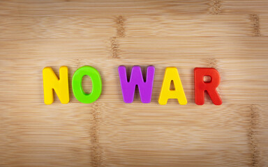 The words no war is laid out of multicolored letters on a table background with a wood texture. Concept. Peace. Stop war