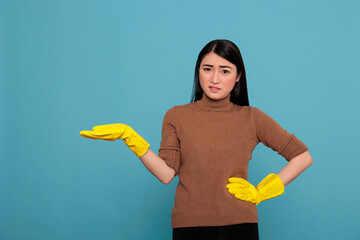 Unhappy tired and overworked asian housewife from chores disgusted expression pointed her hand aside at the free space and wearing yellow glove, Cleaning home concept, Negative state of mind