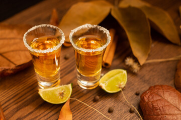 Tequila, shots with autumn decoration, with dry leaves on wooden table