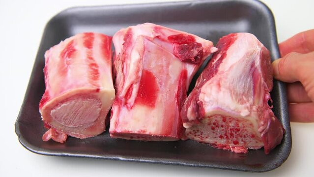 Macro closeup of hand holding beef marrow bones in package container with red uncooked raw meat isolated against white background table