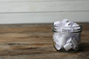 Glass jar with paper pieces on wooden table, space for text