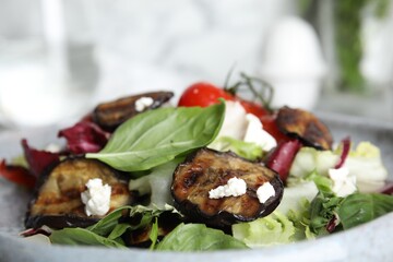 Delicious salad with roasted eggplant, basil and cheese on plate, closeup