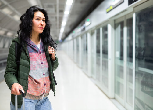 Portrait of young adult woman with luggage waiting for subway car at station