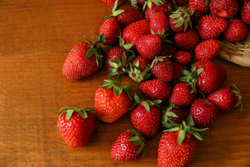 Basket with scattered ripe strawberries on wooden table, top view