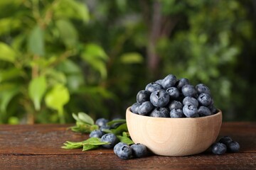 Tasty fresh blueberries and green leaves on wooden table outdoors, space for text