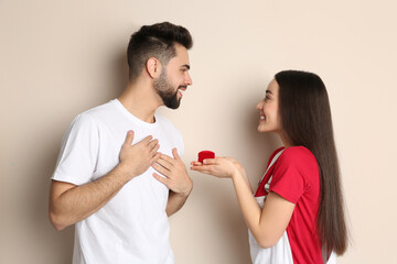 Young woman with engagement ring making marriage proposal to her boyfriend on beige background