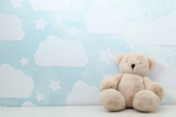 Teddy bear on white table near wall with blue sky, space for text. Baby room interior