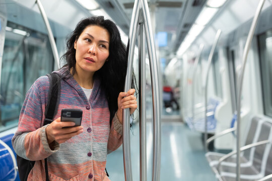 Portrait of young woman commuting in city using tube, checking subway route map in smartphone
