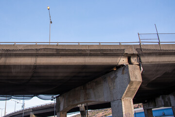 A concrete bridge over a two lane highway. The high overpass has a metal handrail. Black...