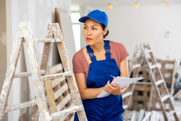 Asian woman worker checking documents during repair works indoors.