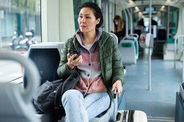 Oriental woman traveler rides a tram and talks on a mobile phone