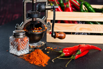 finely ground red hot pepper, mill and pepper pods on a black table.