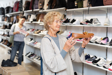 Fototapeta na wymiar Portrait of a mature european woman choosing loafers, standing near the shelves with goods in a shoe store