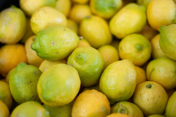 A dark colored basket, black,  filled with oblong shaped lemons at a farmer's market. The juicy vibrant yellow thick peel of the citrus has a tint of green around the pedicle of the ripe sour fruit. 