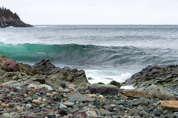 An angry turquoise green color massive rip curl of a wave as it barrels rolls along the ocean. The white mist and froth from the wave are foamy and fluffy. The ocean in the background is deep blue. 
