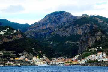 Fototapeta na wymiar Colorful scene in Amalfi coast with a ridge of momentous mountains standing high above some terracing and with a densely populated area in the lower part full of original buildings and some boats