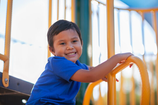 Young Latino boy looking down and smiling while having fun climbing a jungle gym monkey bar.