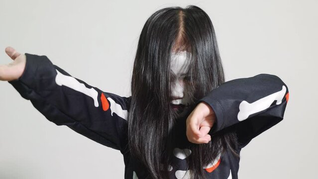 Asian little kid girl with face painting and hair covering face, woman child ghost or zombie horror creepy scary skeleton costume studio shot isolated on white background, Happy Halloween day concept