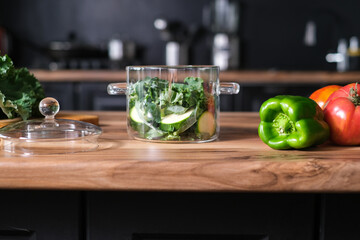 Stylish cooking glass pot with green vegetables in kitchen table.