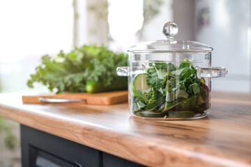 Stylish cooking glass pot with green vegetables in kitchen table.