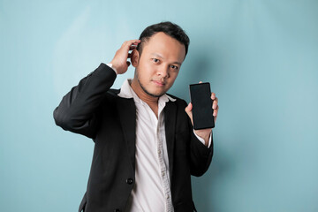 A portrait of a happy Asian businessman is smiling and holding his smartphone showing copy space on it's screen wearing black suit isolated by a blue background