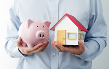 Man holding piggy bank and miniature house. Concept image of saving family budget.