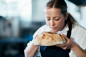 Baker, pastry chef and cafe owner smelling a loaf of fresh baked bread in the kitchen of her coffee shop. Closeup of a female cook enjoying the aroma of a freshly made dough treat or consumables - Powered by Adobe