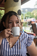 Latin young woman in coffee shop drinking coffee