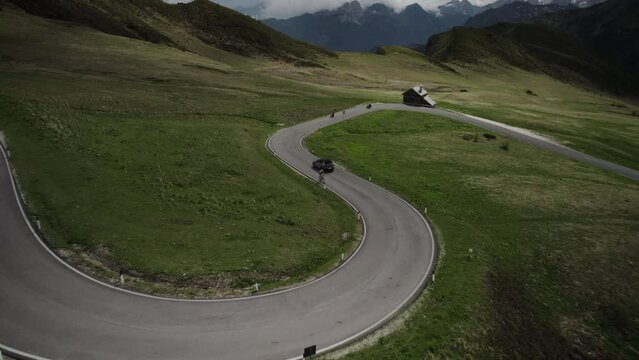 Car drives down curvy Giau Pass past motorcycles in scenic Dolomites; drone