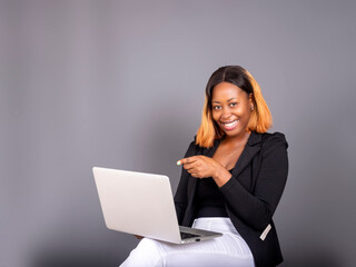 Happy african American young woman holding newest laptop and pointing at it looking at camera isolated over a Grey studio background