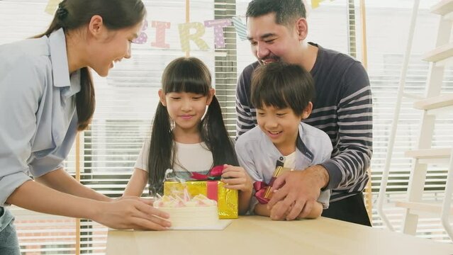 Happy Asian Thai Family, Young Kids Surprised By Birthday Cake, Gift, Blow Out A Candle, And Celebrate Party With Parents And Siblings Together At Dining Table, Wellbeing Domestic Home Special Event.