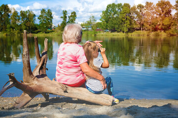 Fototapeta na wymiar Little girl with her grandmother looking through binoculars outdoor. Travel, hiking, vacations