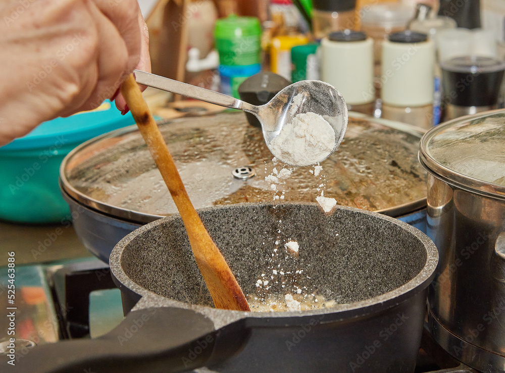 Wall mural chef throws flour into pot of bechamel sauce being prepared on gas stove