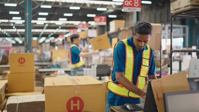 Warehouse worker using a QR code reader, scanning parcels into the system while working inside a large distribution center, worker checking goods packages and making inventory of goods.