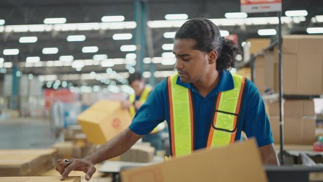 Warehouse worker using a QR code reader, scanning parcels into the system while working inside a large distribution center, worker checking goods packages and making inventory of goods.